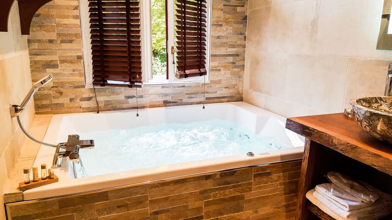 Suite Indonésienne : jacuzzi en bulles sous la fenêtre aux stores de bois et vasque en pierre