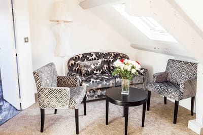 Suite Vue sur Ciel : coin salon mansardé, canapé fleuri, fauteuils et bouquet de roses sur la table