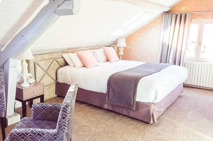 Suite Vue sur Ciel : chambre mansardée, poutres claires, lit et coussins roses sous la fenêtre de toit
