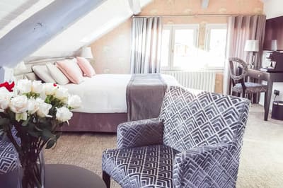 Suite Vue sur Ciel : bouquet de roses, fauteuil à motifs et lit sous les poutres