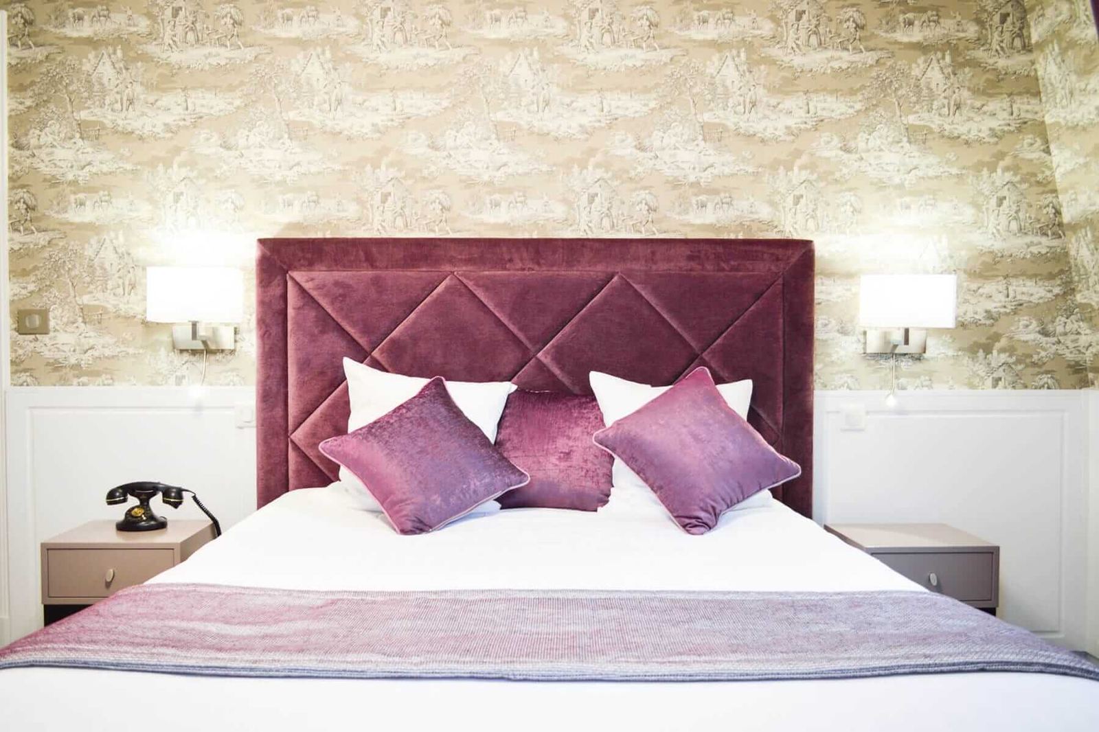 Suite Royale : tête de lit capitonnée prune, coussins violets et téléphone rétro au chevet
