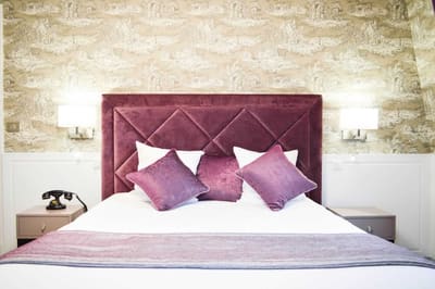 Suite Royale : tête de lit capitonnée prune, coussins violets et téléphone rétro au chevet