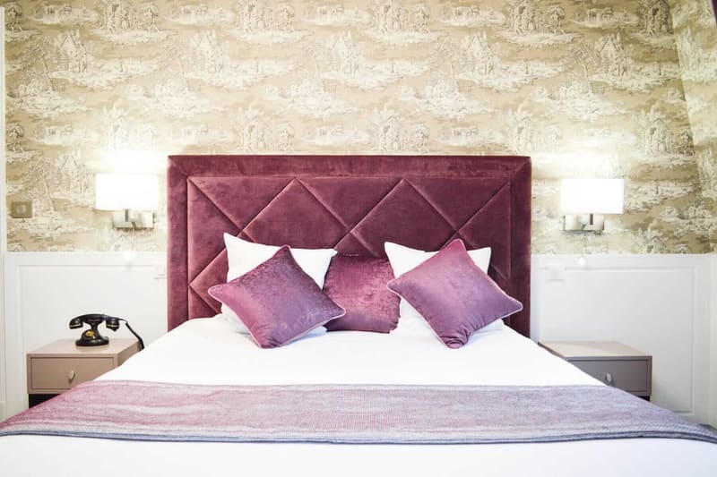 Suite Royale : tête de lit capitonnée prune, coussins violets et téléphone rétro au chevet