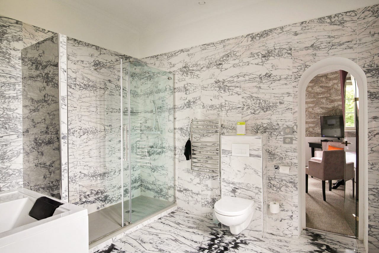 Suite Royale : douche vitrée et sèche-serviettes dans le marbre, passage voûté vers la chambre
