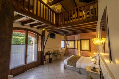 Suite Familiale Licorne : vaste pièce à mezzanine, poutres apparentes et porte-fenêtre sur le jardin