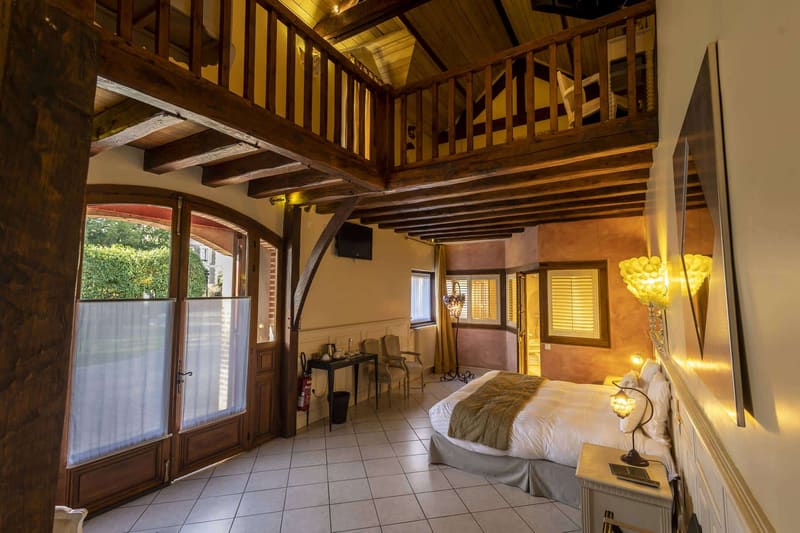Suite Familiale Licorne : vaste pièce à mezzanine, poutres apparentes et porte-fenêtre sur le jardin