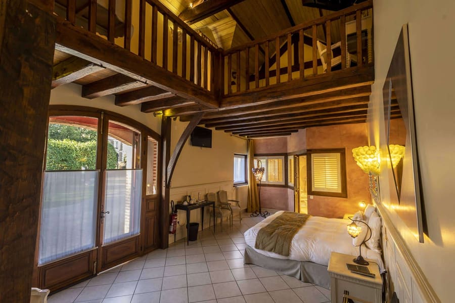 Suite Familiale Licorne : vaste pièce à mezzanine, poutres apparentes et porte-fenêtre sur le jardin