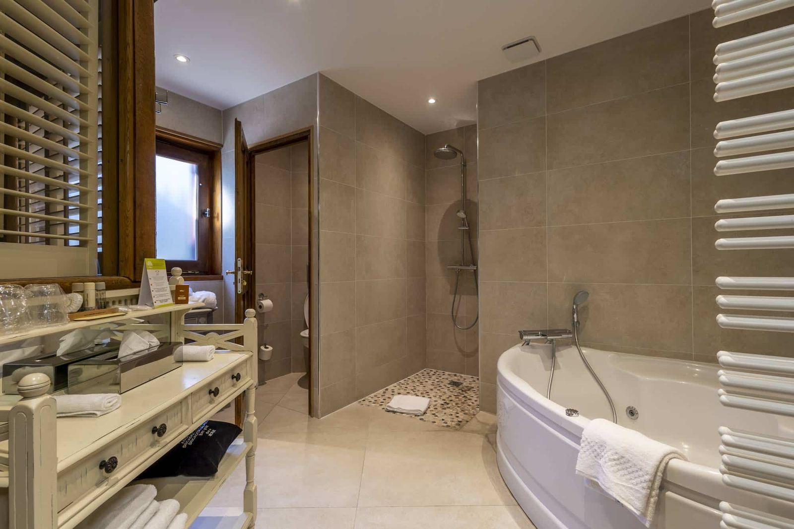 Suite Familiale Licorne : baignoire d’angle, douche, console blanche et serviettes, carrelage beige