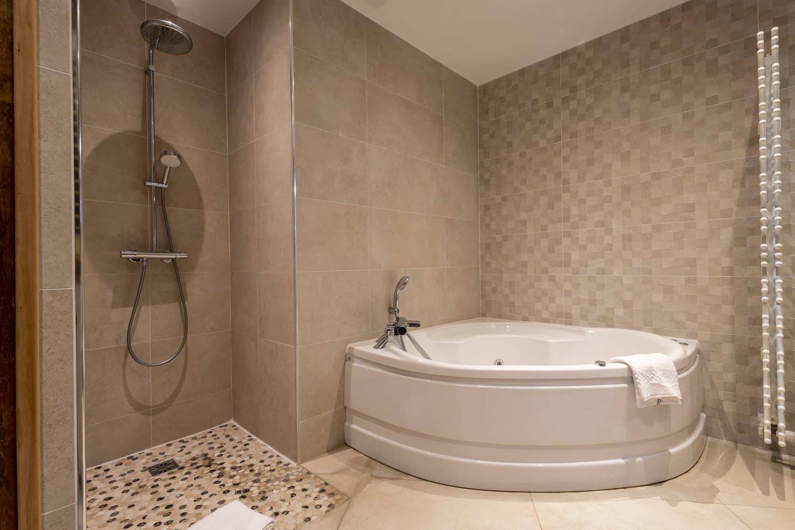 Suite Familiale Licorne : baignoire d’angle et douche à l’italienne au sol de galets, carrelage beige
