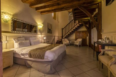 Suite Familiale Licorne : lit, escalier en bois vers la mezzanine et fauteuils sous les poutres