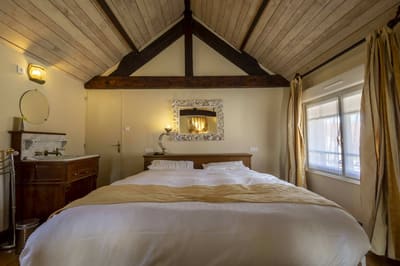 Suite Familiale Licorne : grand lit sous la charpente, jeté doré, miroir baroque et lavabo ancien
