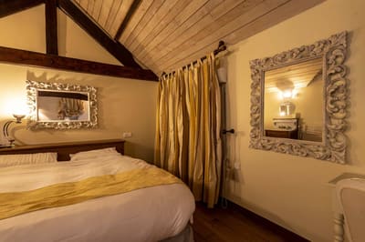 Suite Familiale Licorne : lit au jeté jaune, rideau rayé et miroir baroque sous les poutres
