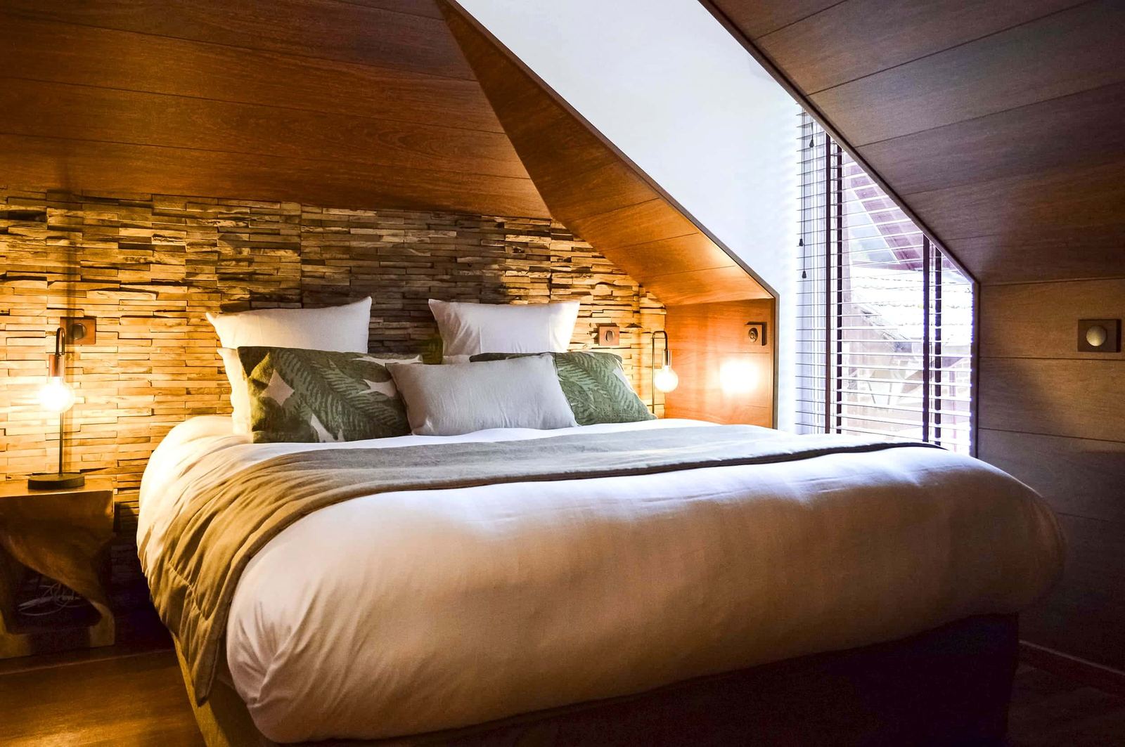 Suite Indonésienne : grand lit sous les combles, mur de bois brut et fenêtre à stores
