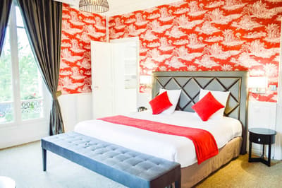 Suite Princière : lit à tête capitonnée grise, banquette, plaid rouge et toile de Jouy rouge