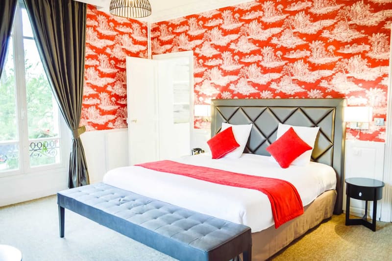 Suite Princière : lit à tête capitonnée grise, banquette, plaid rouge et toile de Jouy rouge