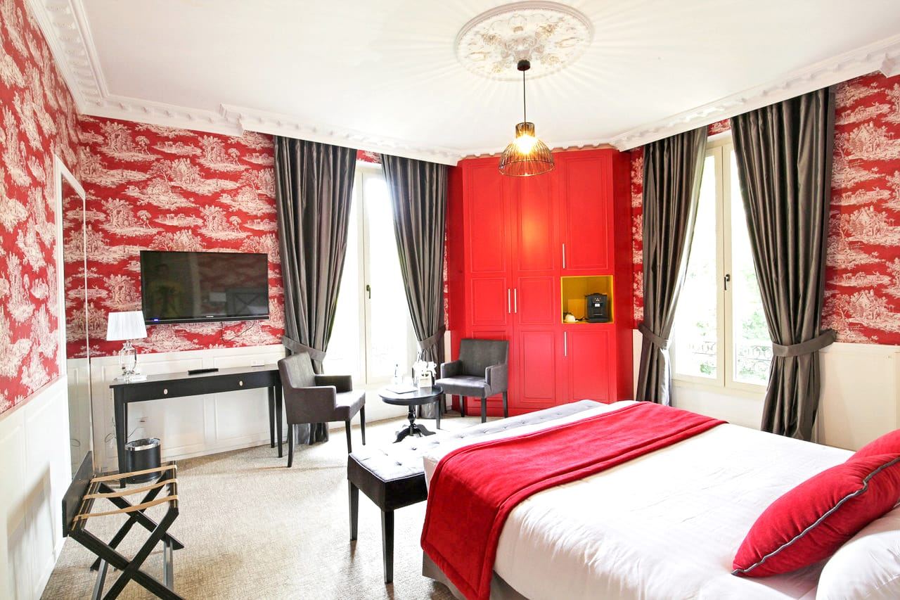 Suite Princière : chambre rouge et blanche, armoire rouge, lit et coin salon entre deux fenêtres