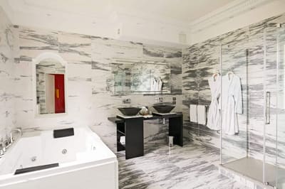 Suite Princière : salle de bains en marbre avec jacuzzi, double vasque noire et douche vitrée